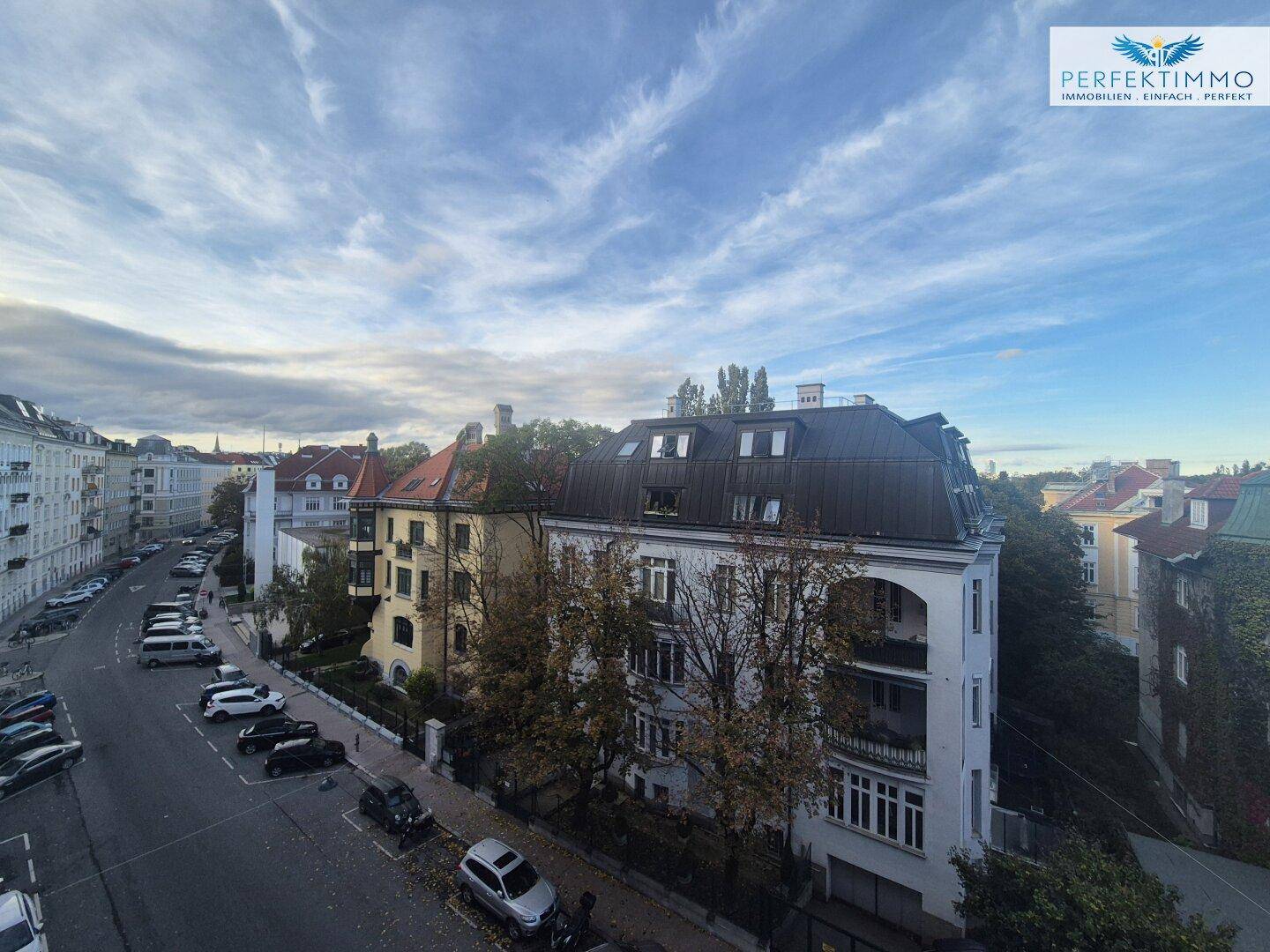 Weitläufiger Blick über die Dächer der Stadt mit parkenden Autos auf der Straße unter einem bewölkten Himmel.