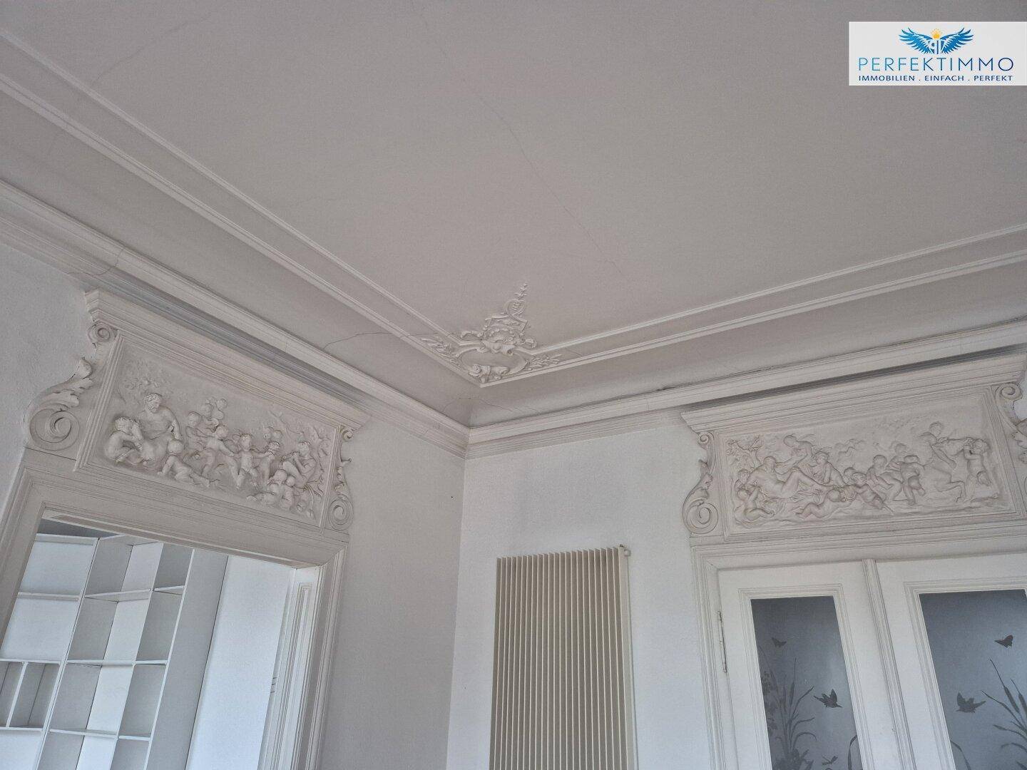Detailaufnahme der kunstvollen Stuckdecke und der reich verzierten Türrahmen, die den historischen Charakter betonen.