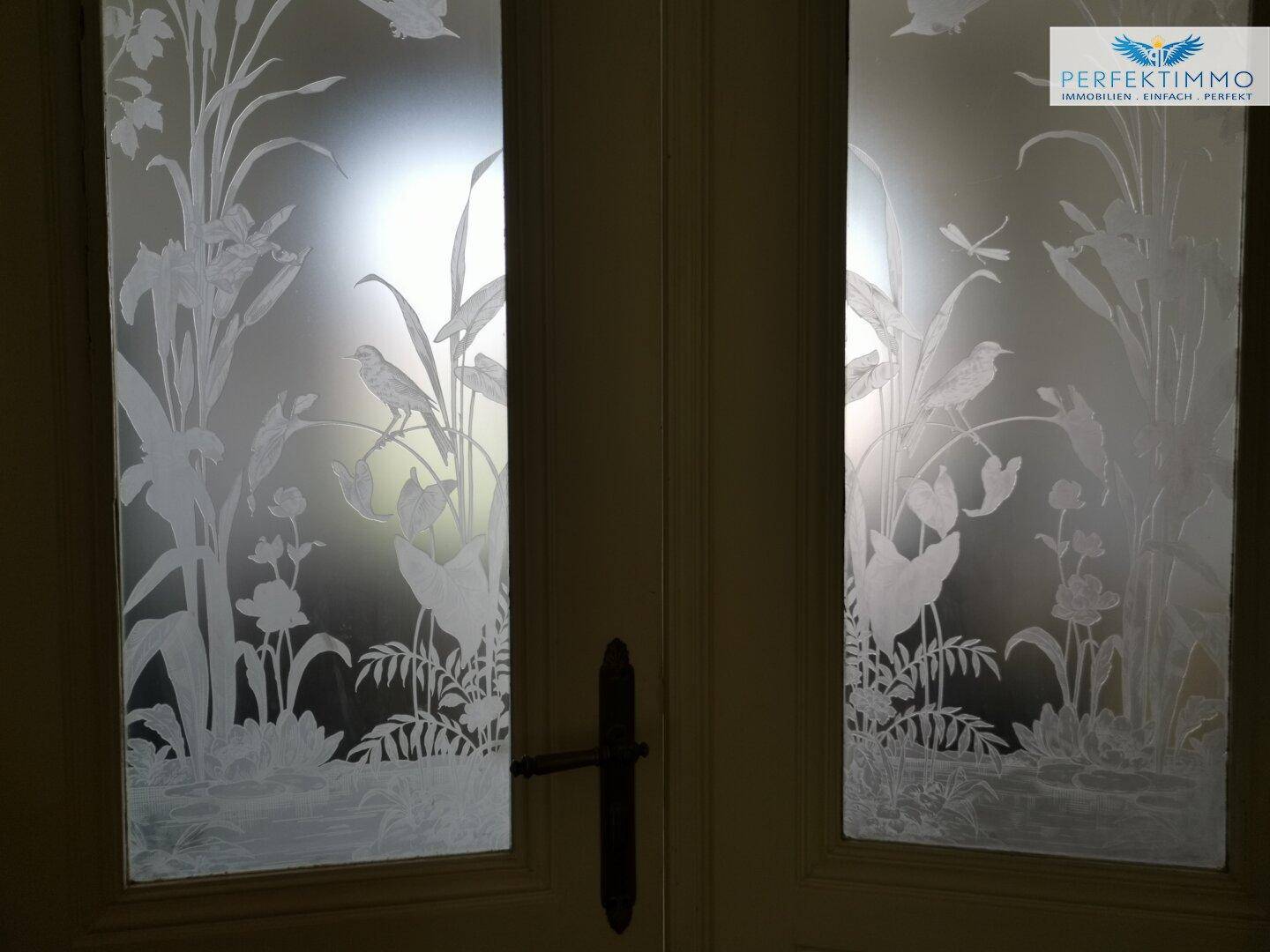 Nahaufnahme der geätzten Glastüren mit detaillierten Pflanzen- und Tiermotiven, die ein elegantes Design zeigen.
