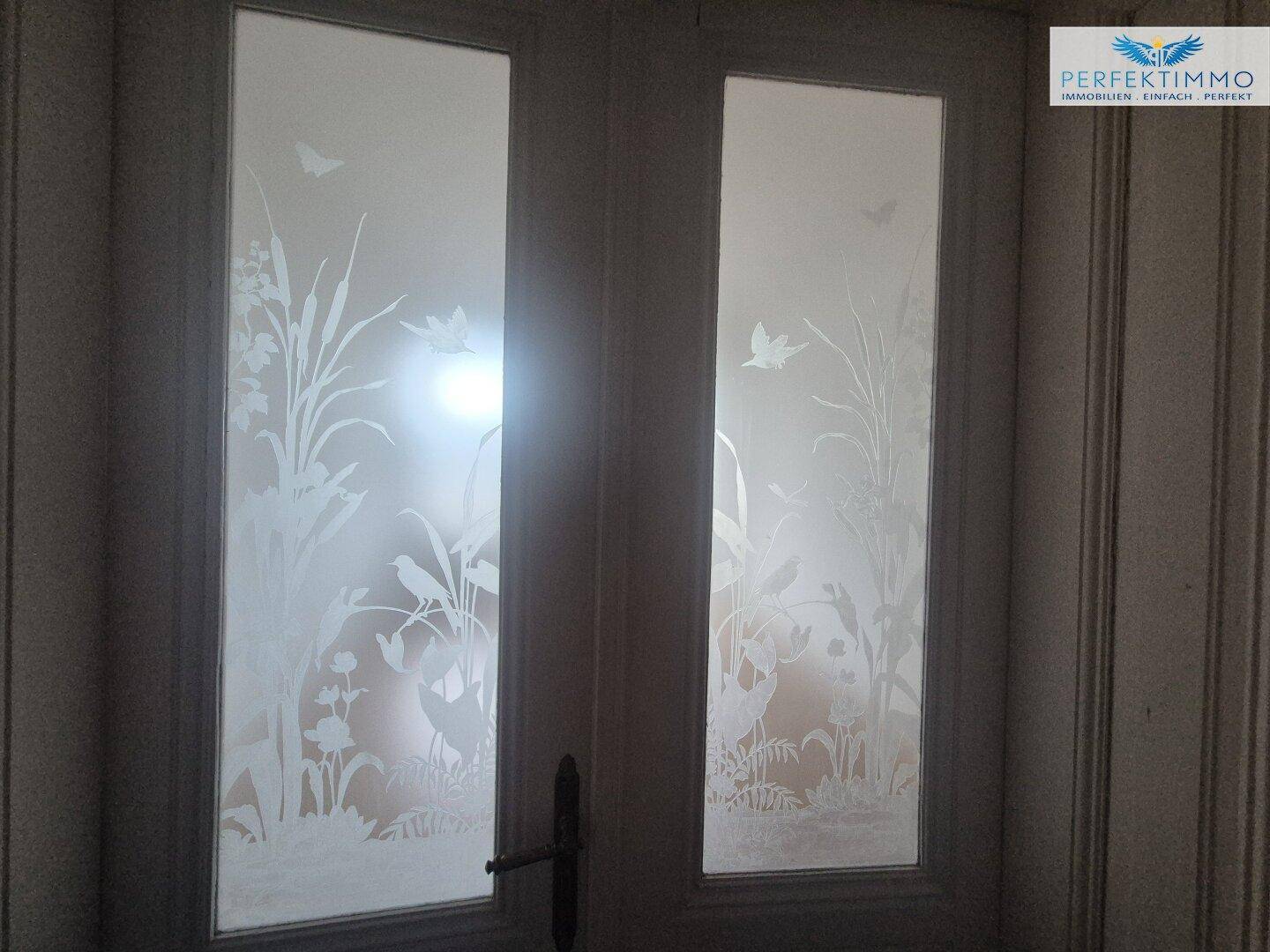 Detailansicht von Glastüren mit kunstvollen, geätzten floralen Mustern und Vogelmotiven.