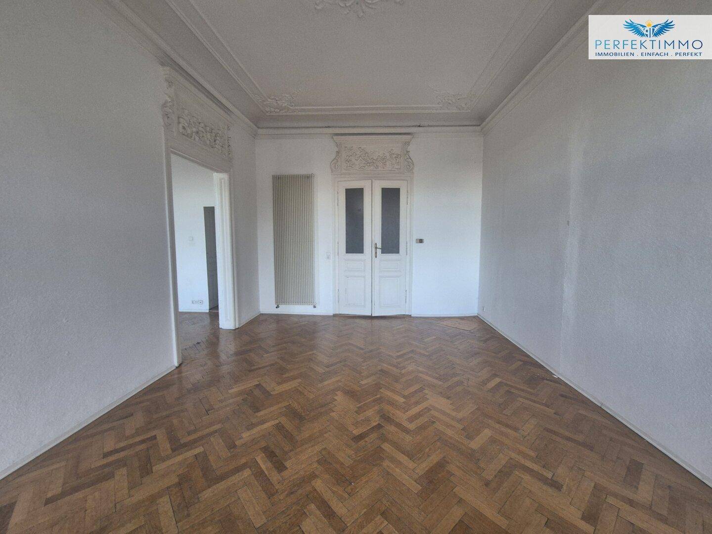 Geräumiges Zimmer mit Fischgrätparkett, hohen Decken und klassischen Türen, bereit zur individuellen Gestaltung.