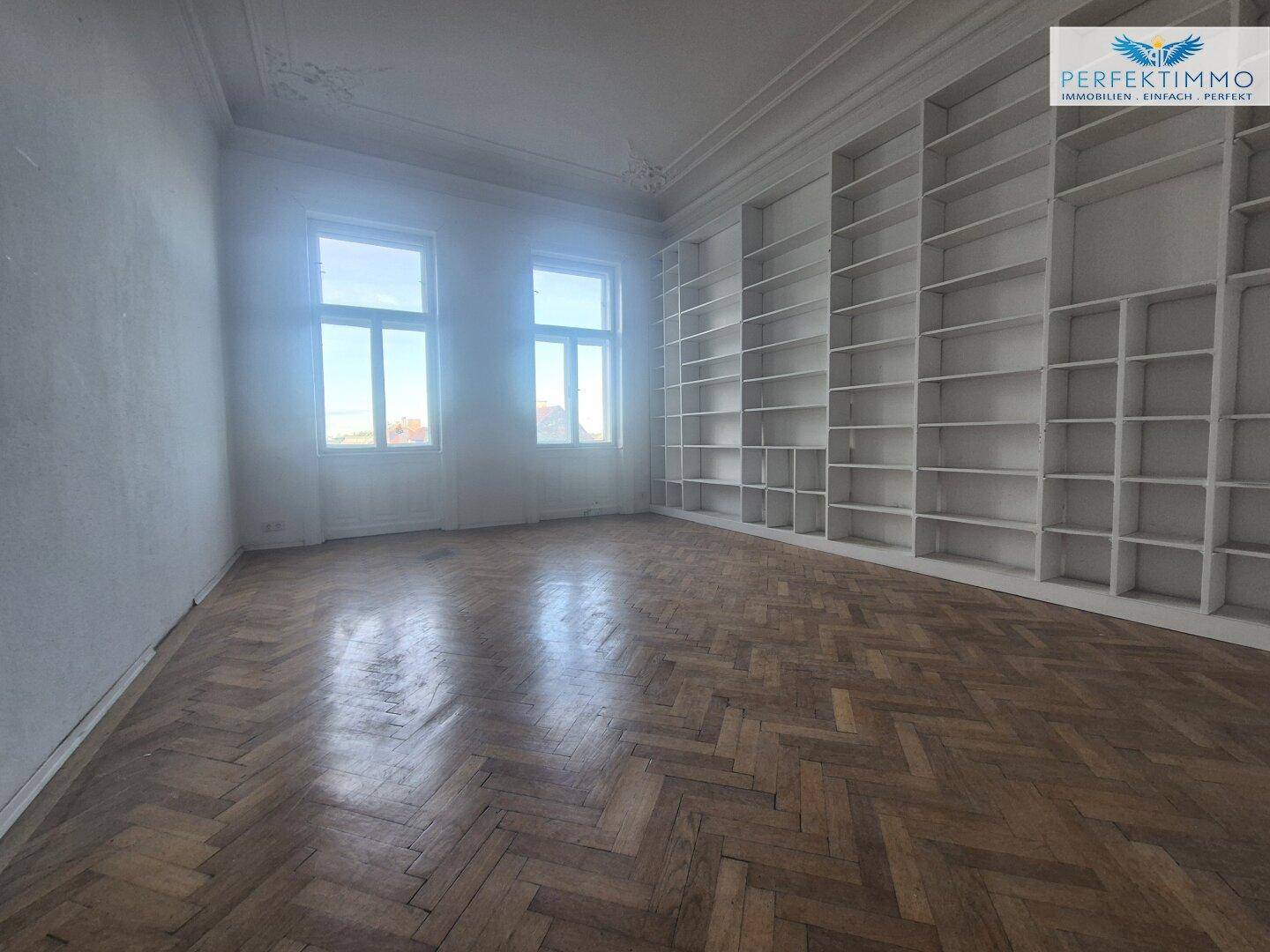 Helles Zimmer mit Fischgrätparkett und einer großen, wandfüllenden Regalwand, ideal für eine Bibliothek.