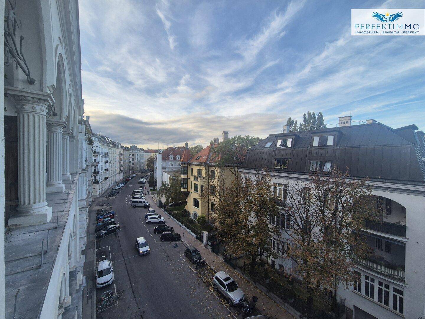 Weitläufige Ansicht einer städtischen Straße mit parkenden Autos und historischen Gebäuden unter blauem Himmel.