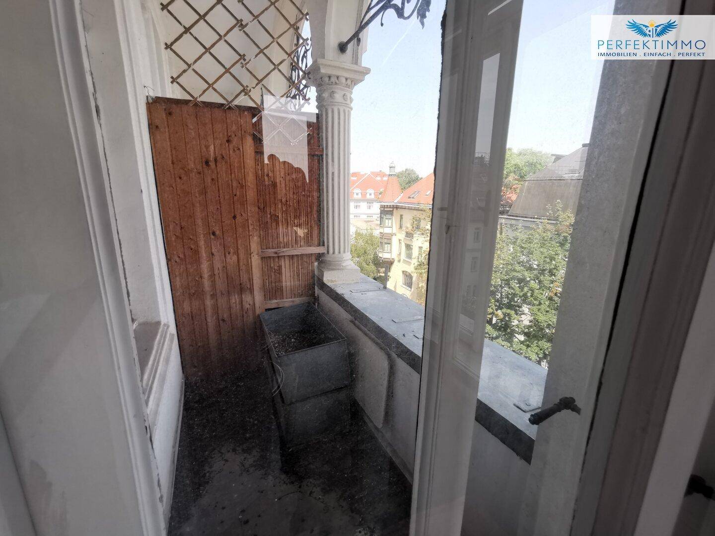 Kleiner, verglaster Balkon mit Holzwänden und Blick auf die umliegenden Gebäude und Bäume.