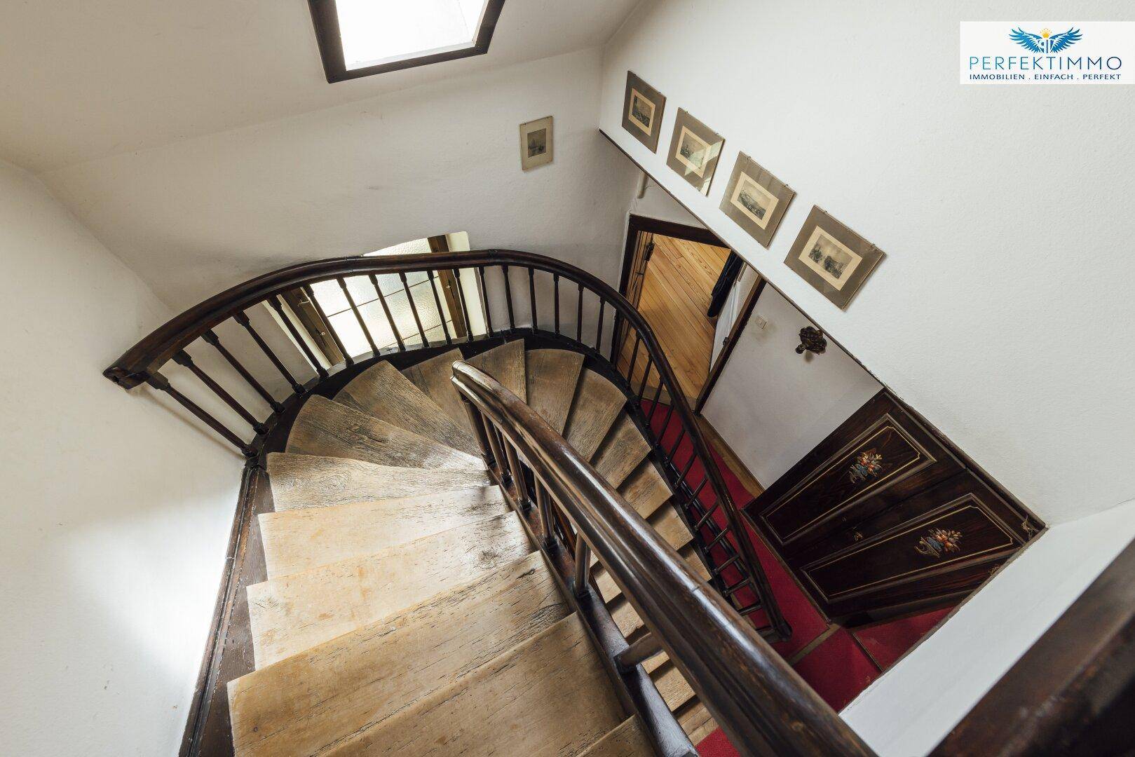 Historisches Treppenhaus mit Holzgeländer und Oberlicht, das in die oberen Stockwerke führt.