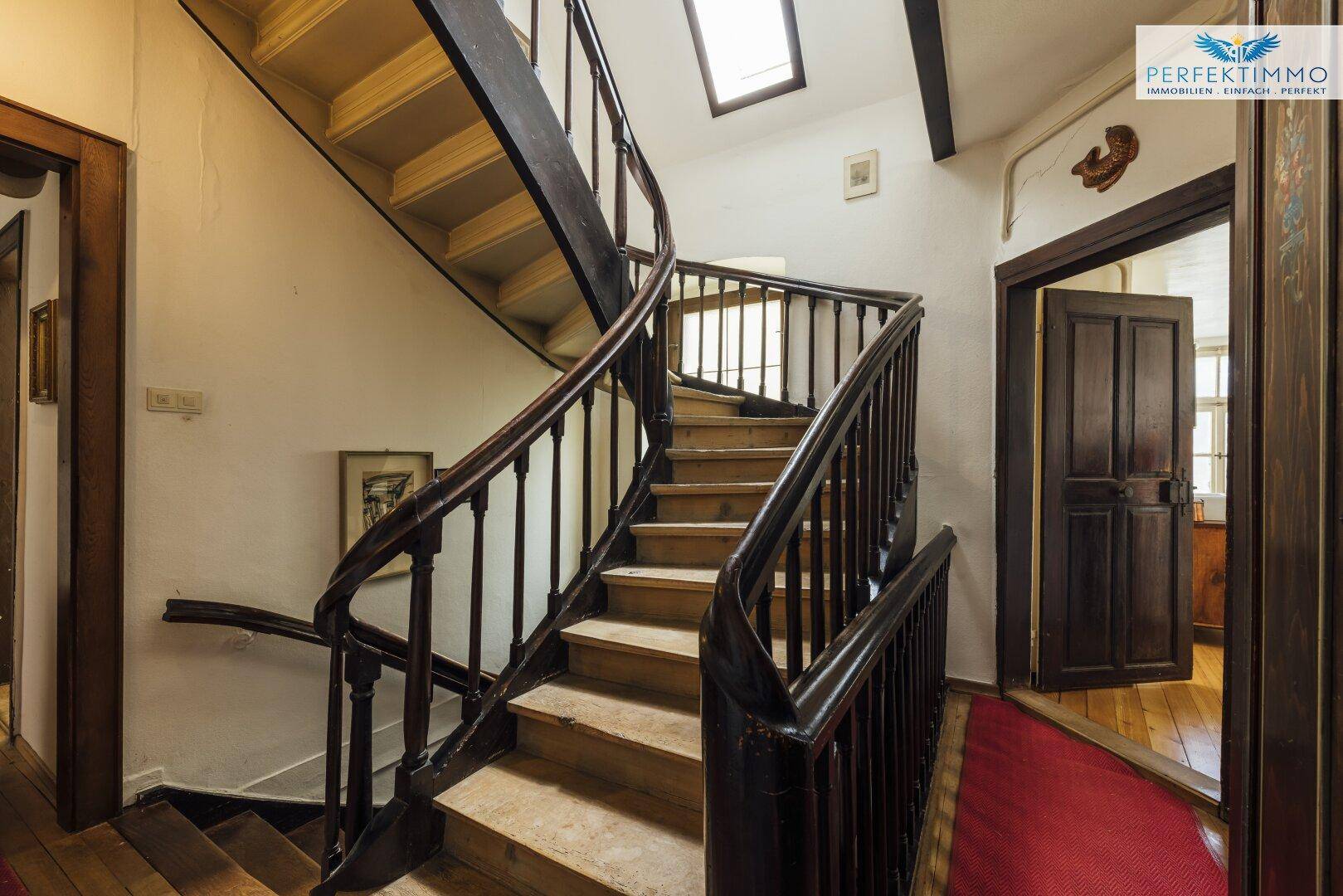 Historisches Treppenhaus mit dunklem Holzgeländer und Zugang zu weiteren Räumen.