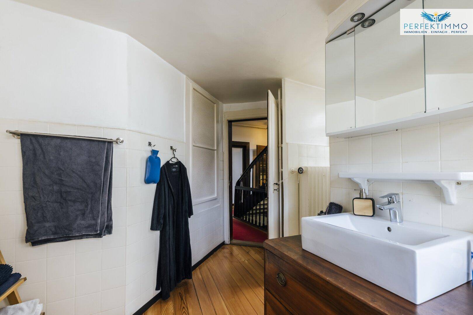 Badezimmer mit Holzfußboden, weiß gefliesten Wänden und Blick auf das Treppenhaus.