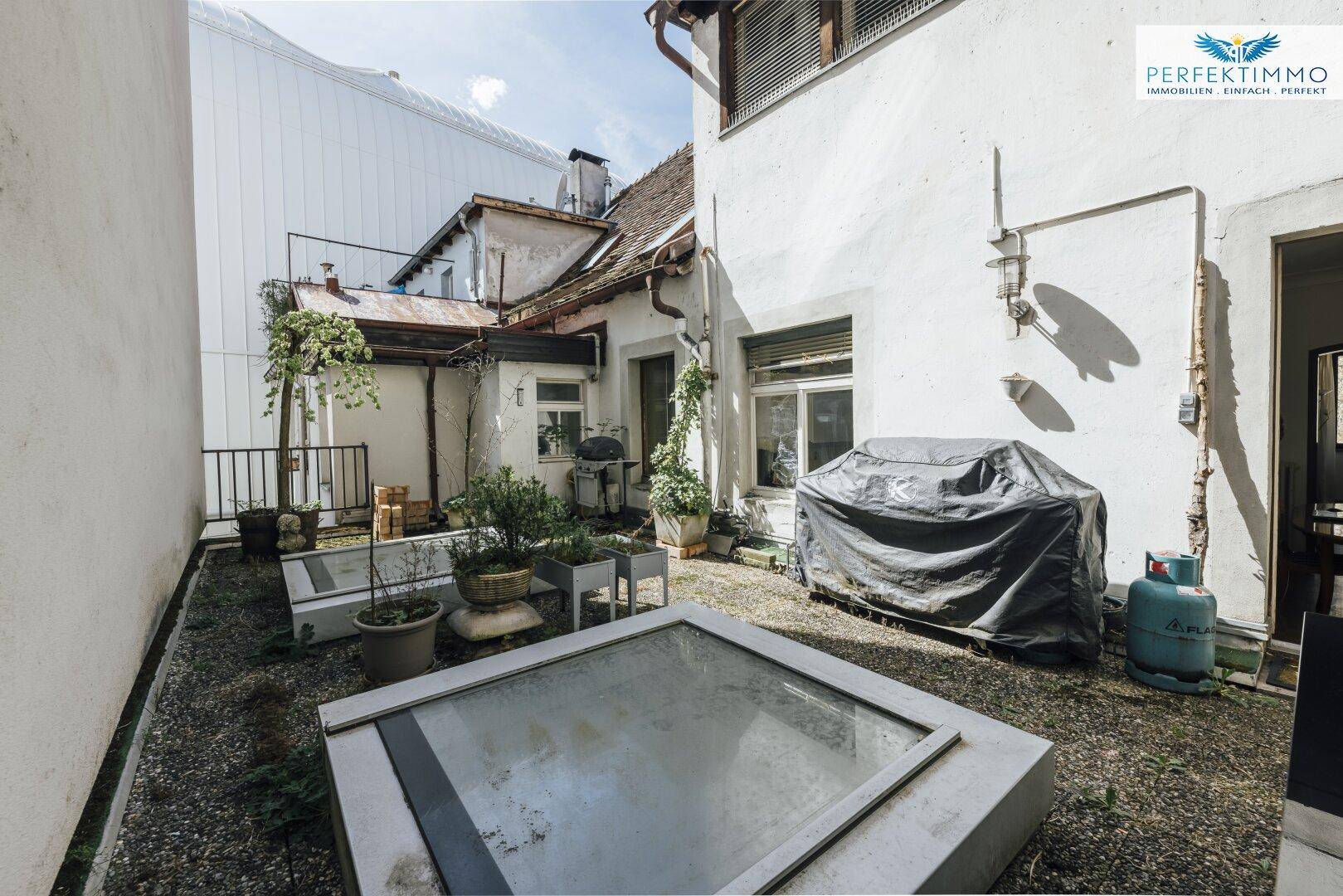 Kleiner Hinterhofgarten mit Kiesboden, Pflanzen und einem Grillbereich.