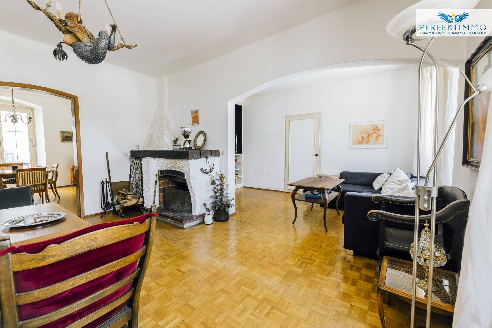Helles Wohnzimmer mit Parkettboden, Kamin und verschiedenen Sitzgelegenheiten.