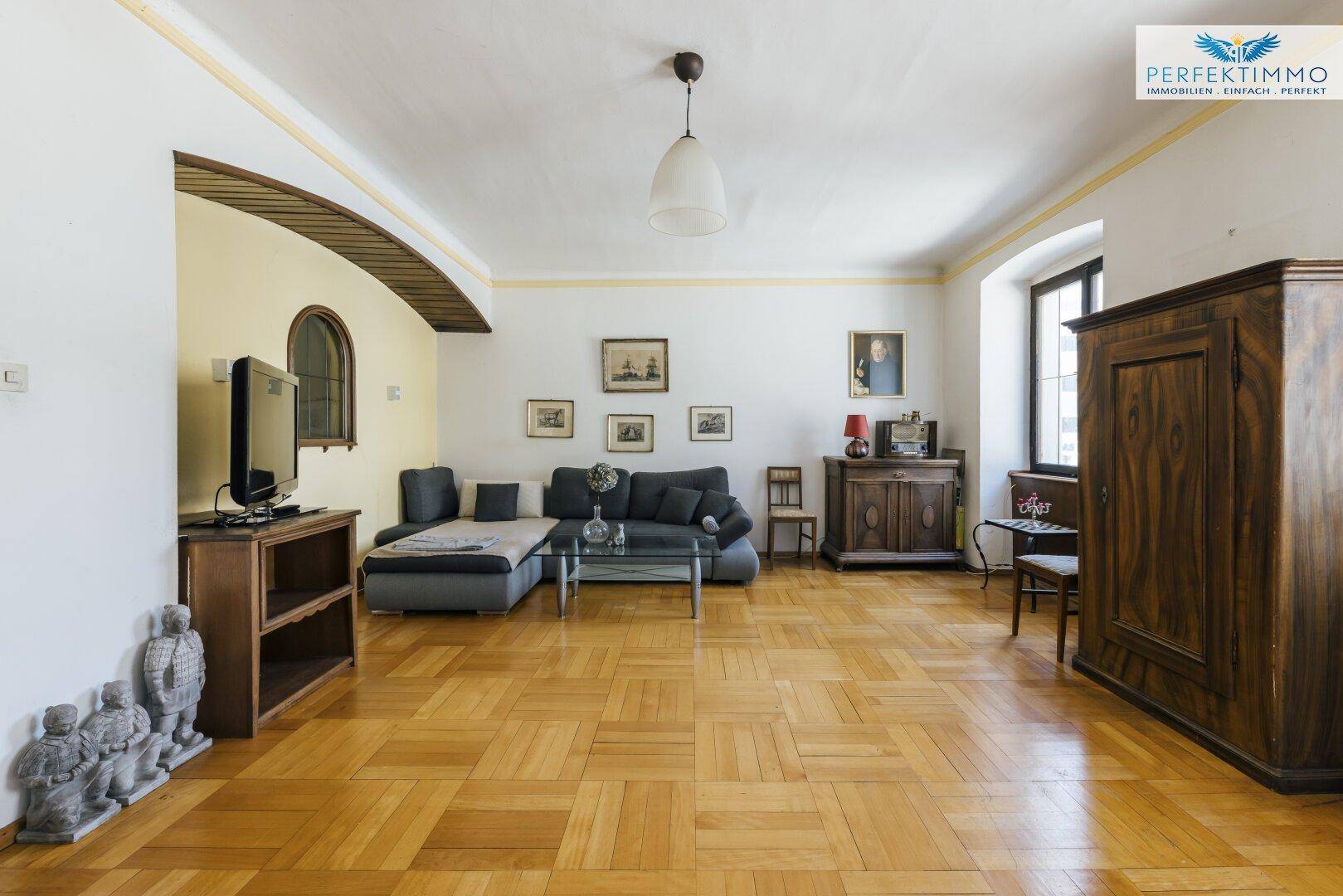 Großes Wohnzimmer mit Parkettboden, Ecksofa und traditionellen Holzmöbeln.
