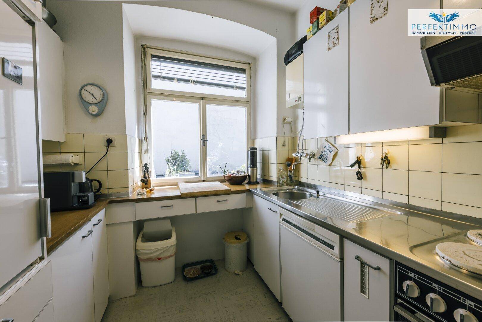 Funktionale Küche mit weißen Schränken, Edelstahlspüle und Fenster.