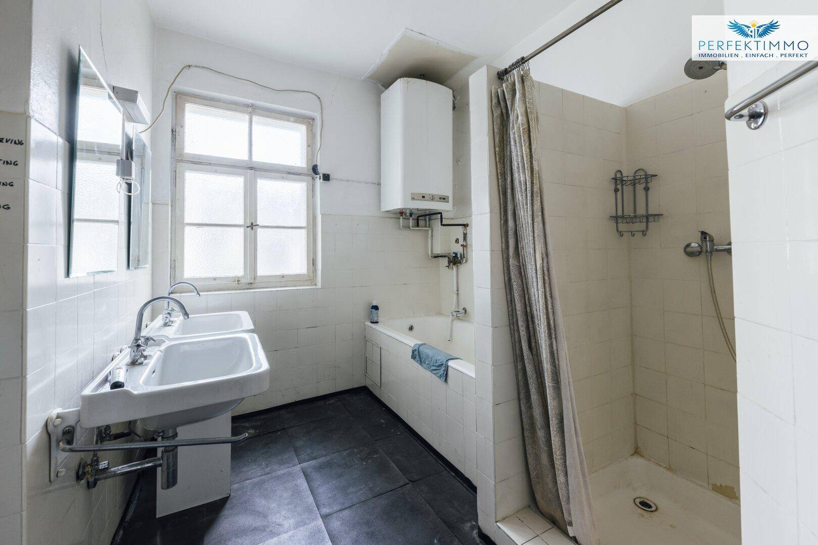 Einfaches Badezimmer mit zwei Waschbecken, Badewanne und Duschvorrichtung.