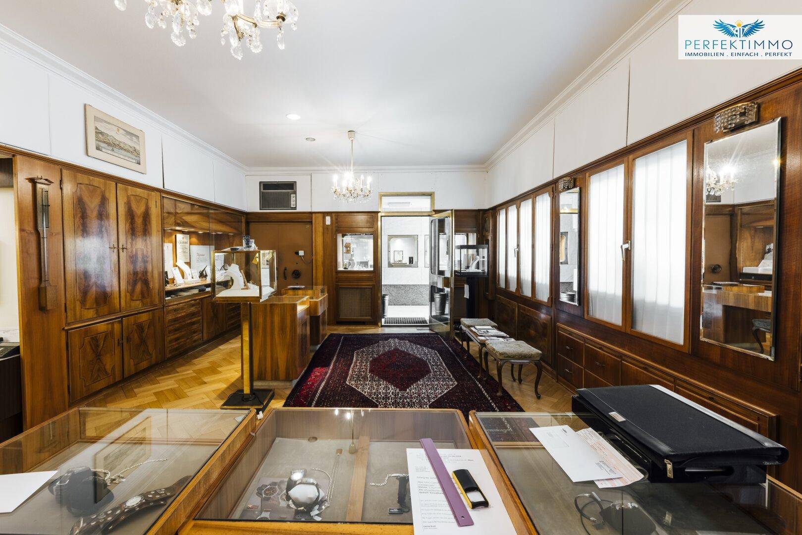 Verkaufsraum mit Holzvitrinen, Parkettboden und eleganten Kronleuchtern.