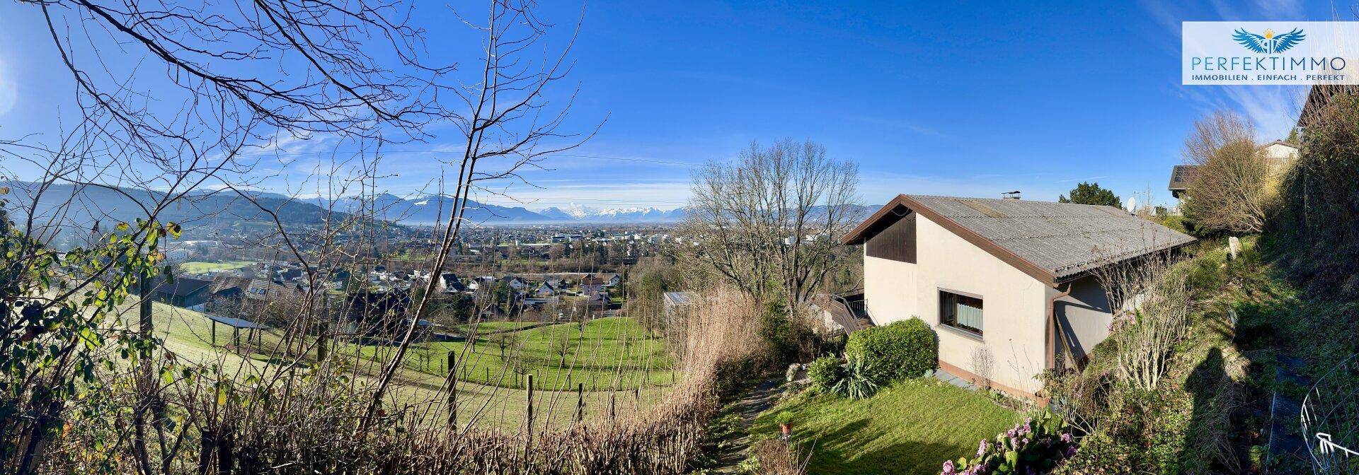 Panoramablick auf das Haus und die weite Landschaft mit Bergen unter strahlend blauem Himmel.