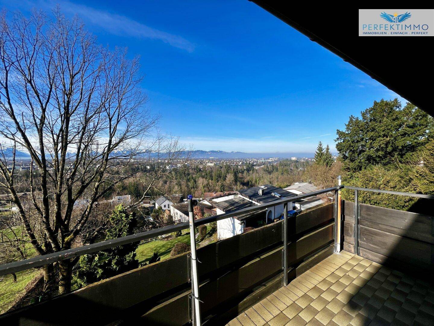 Sonniger Balkon mit Fliesenboden und weitem Blick über die bewaldete Umgebung und die Stadt.