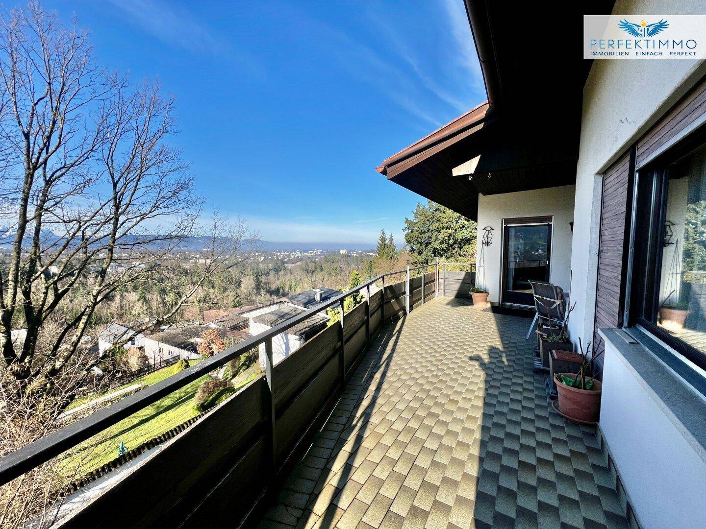 Lange, geflieste Terrasse mit Metallgeländer und Blick auf die umliegende Natur und die Stadt.