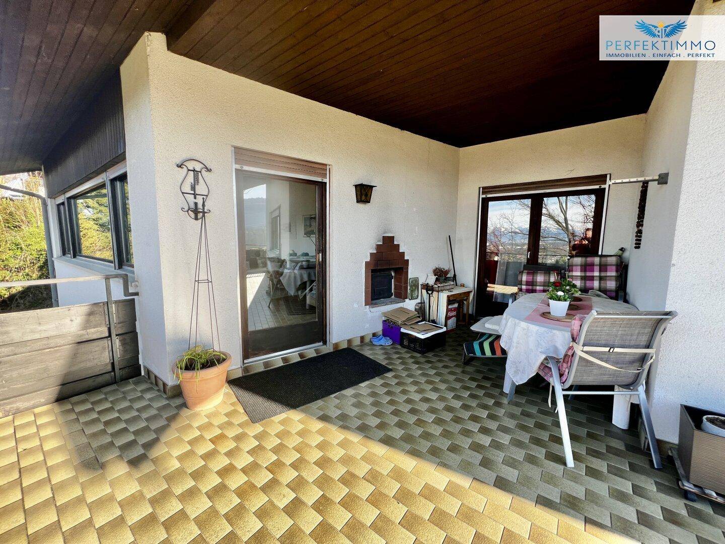 Überdachte Terrasse mit Fliesenboden, Sitzgelegenheiten und einem kleinen Außenkamin.