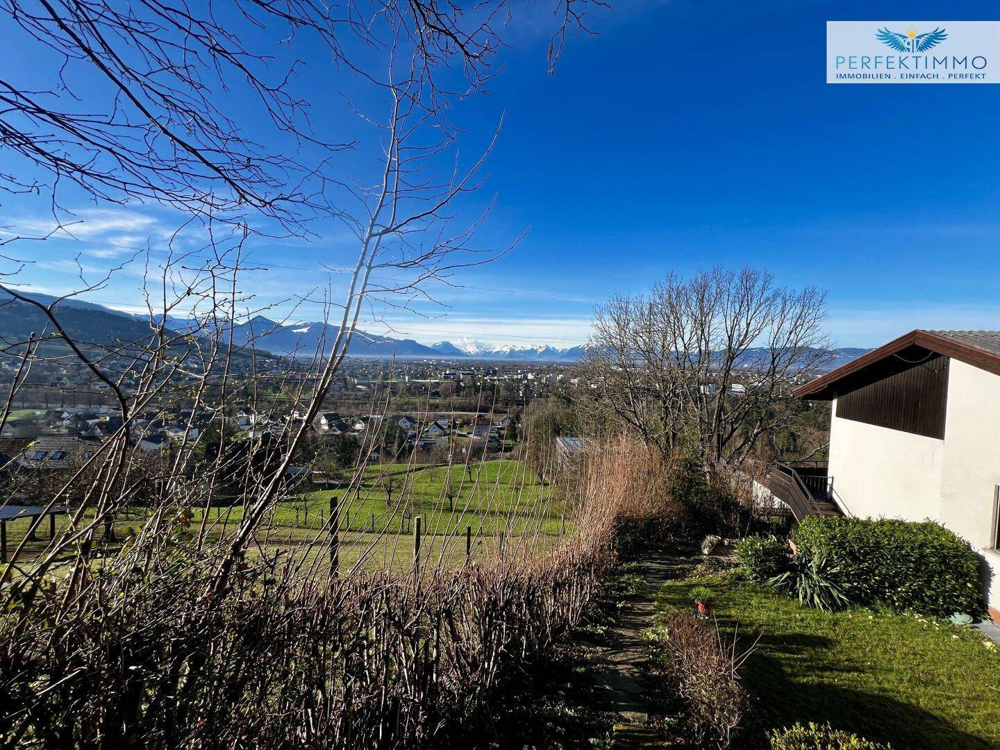 Gartenbereich mit Blick auf die weite Landschaft und die Berge, umgeben von Sträuchern.