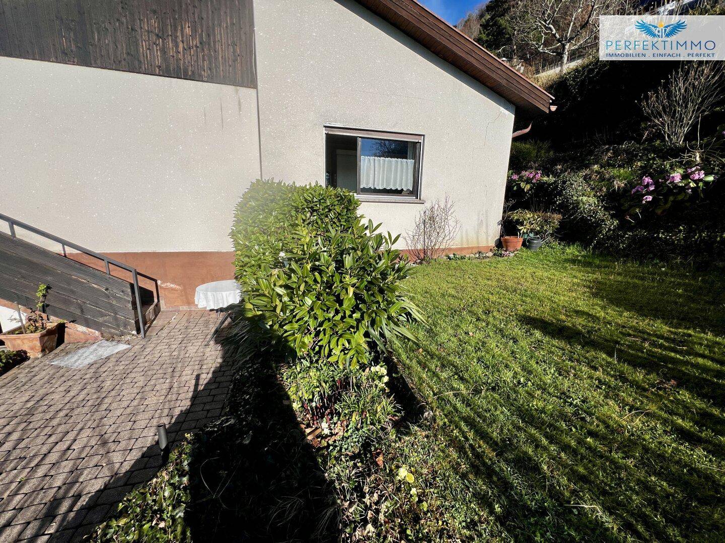 Gepflegter Gartenbereich mit Rasenfläche und einem gepflasterten Weg entlang der Hauswand.