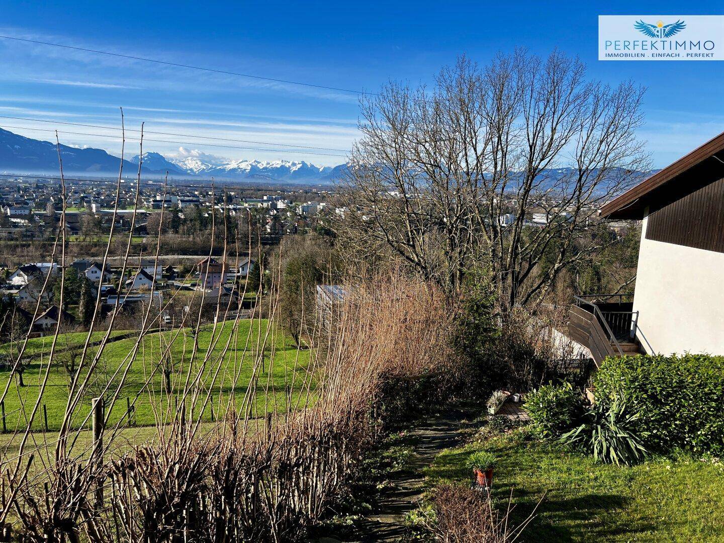 Sonniger Gartenweg mit Blick auf die grüne Landschaft und die fernen Berge.