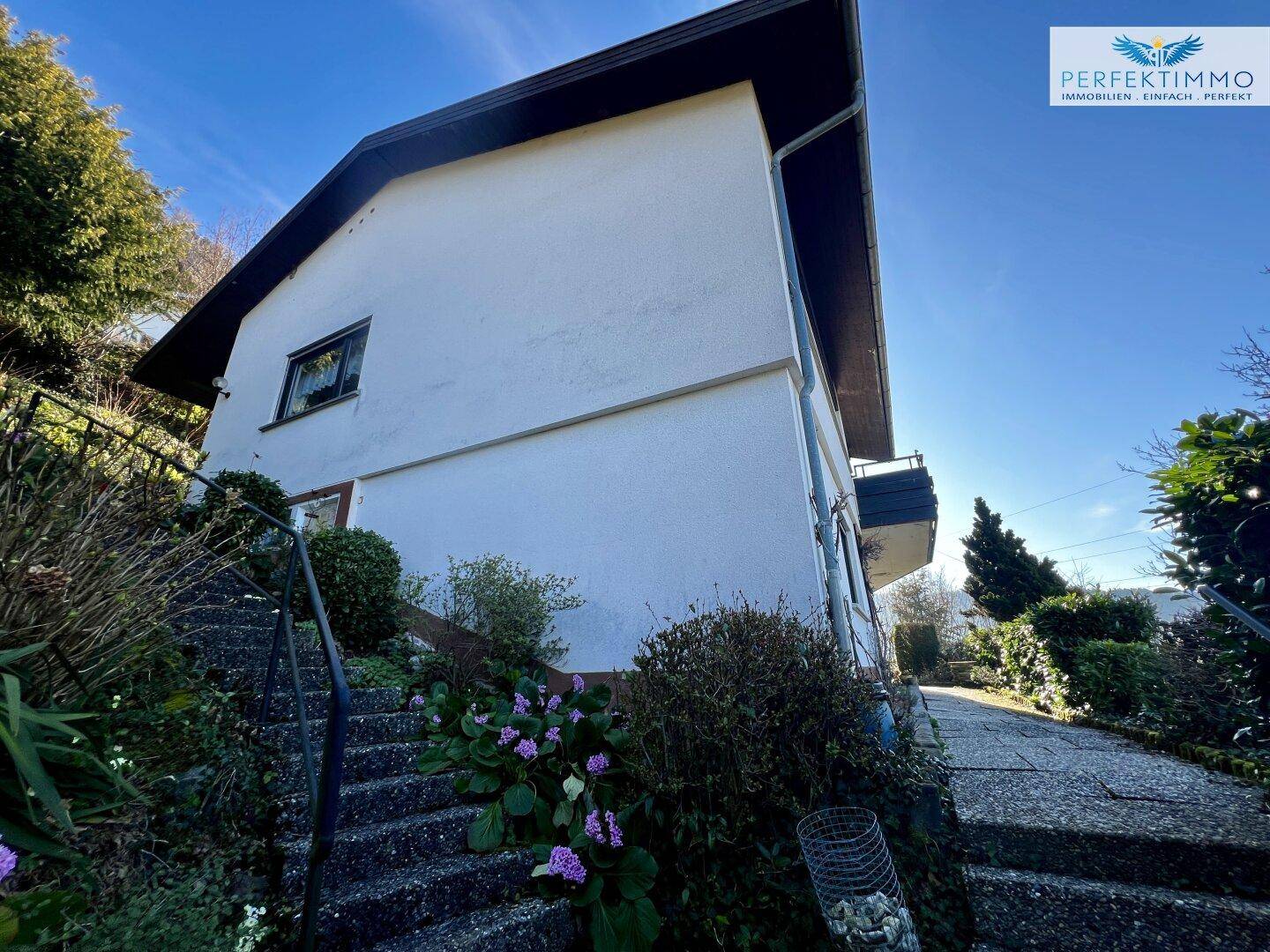 Seitenansicht des Hauses mit Außentreppe und blühenden Pflanzen im Vorgarten.