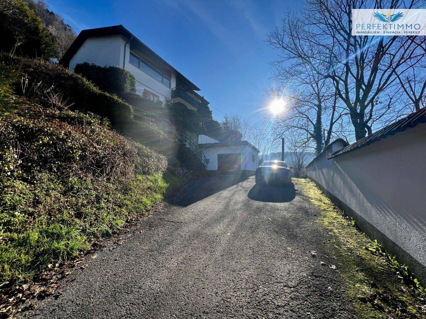 Breite Auffahrt zum Haus mit einem geparkten Auto und sonniger Umgebung.