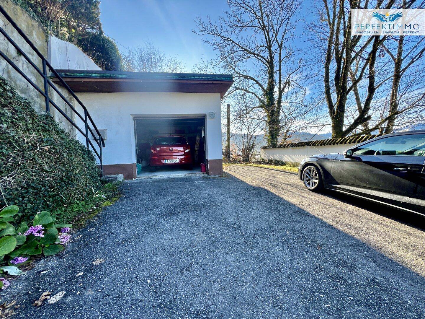 Einzelgarage mit geparktem Auto und asphaltierter Zufahrt vor dem Haus.