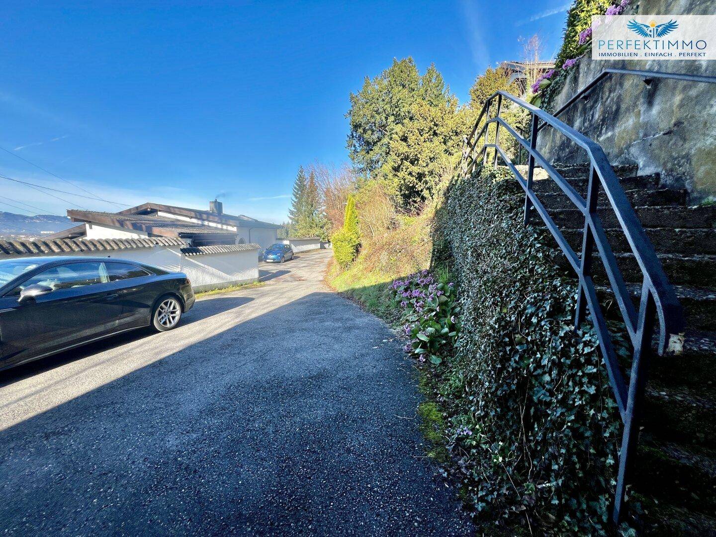 Asphaltierte Auffahrt mit angrenzender Steintreppe und Blick auf die Umgebung.
