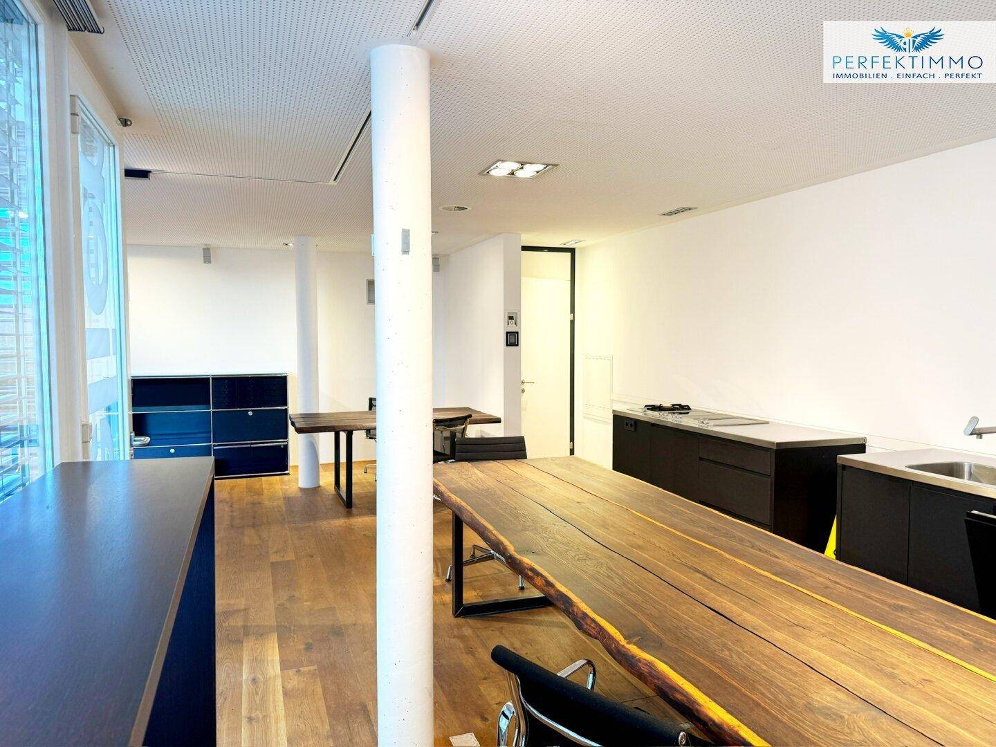 Heller Gewerberaum mit Holzboden, Säule und integrierter Küchenzeile entlang der Wand.