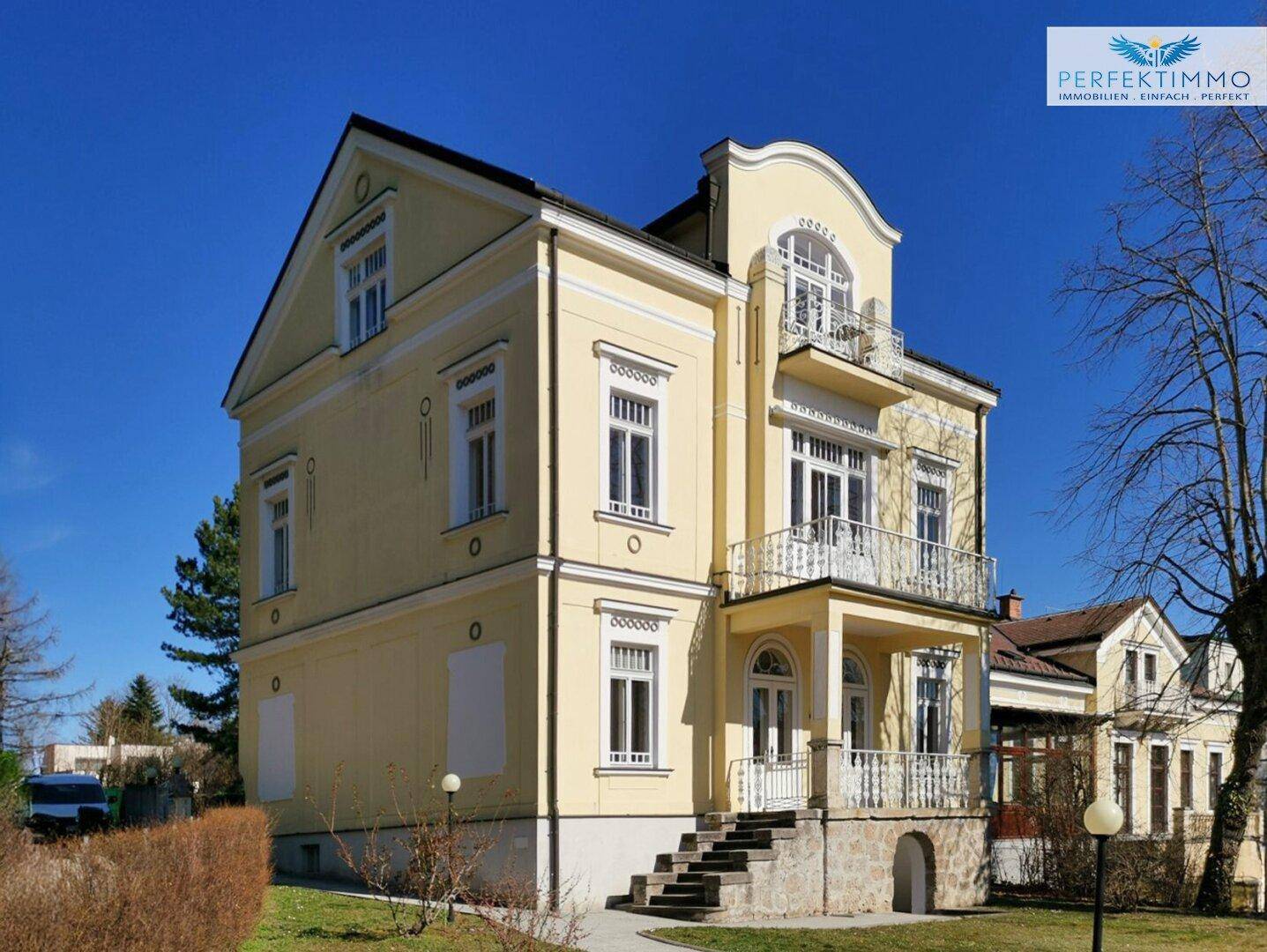 Elegante Fassade der Villa mit Balkonen und dekorativen Elementen unter strahlend blauem Himmel.