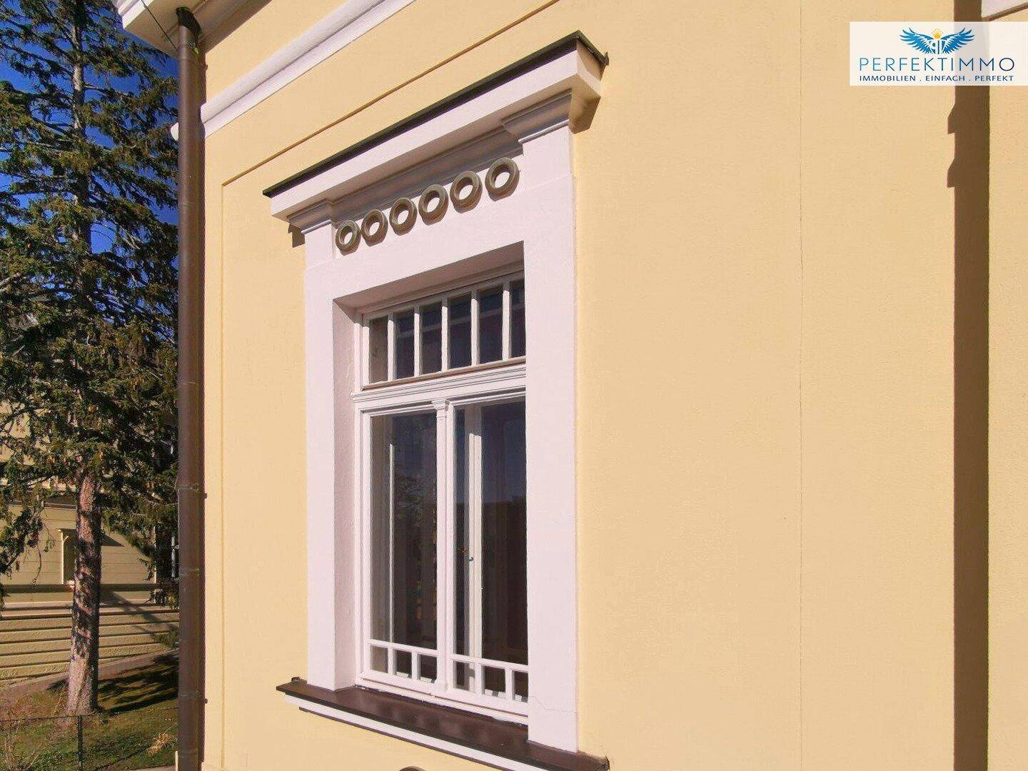 Detail eines Fensters mit dekorativer Umrahmung und Sprossen, typisch für Altbauarchitektur.