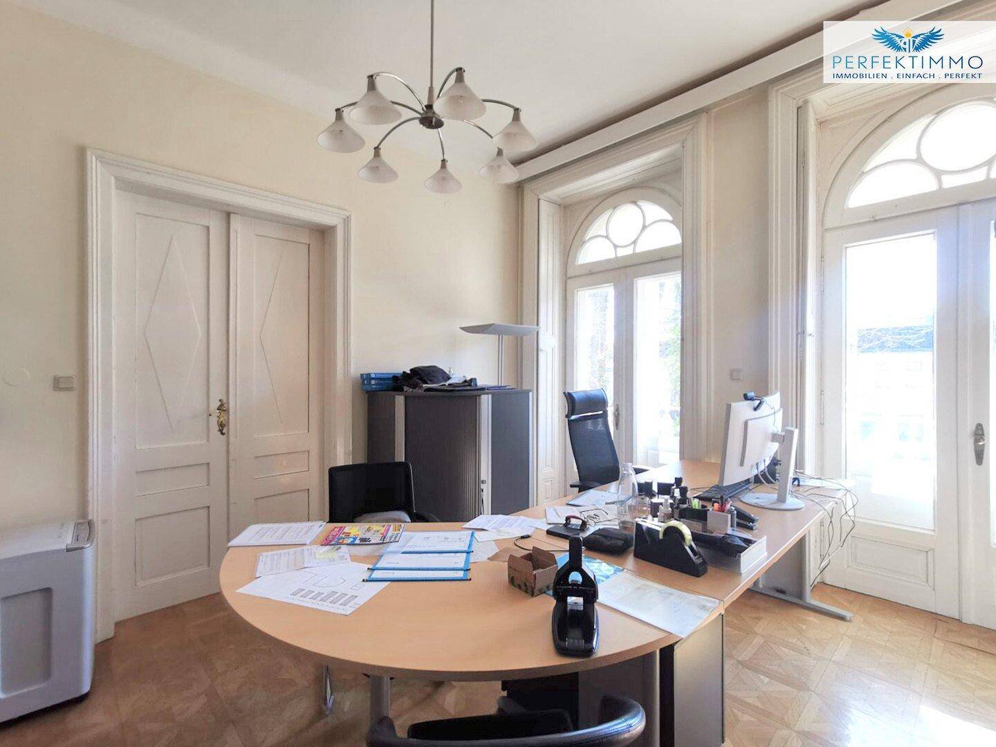 Helles Büro mit großen Fenstern, Parkettboden und klassischer Einrichtung.