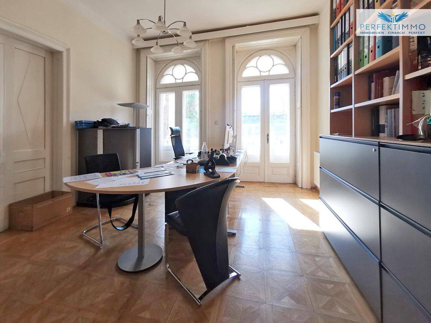 Büro mit Parkettboden, großen Fenstern und einem Bücherregal, das viel Stauraum bietet.