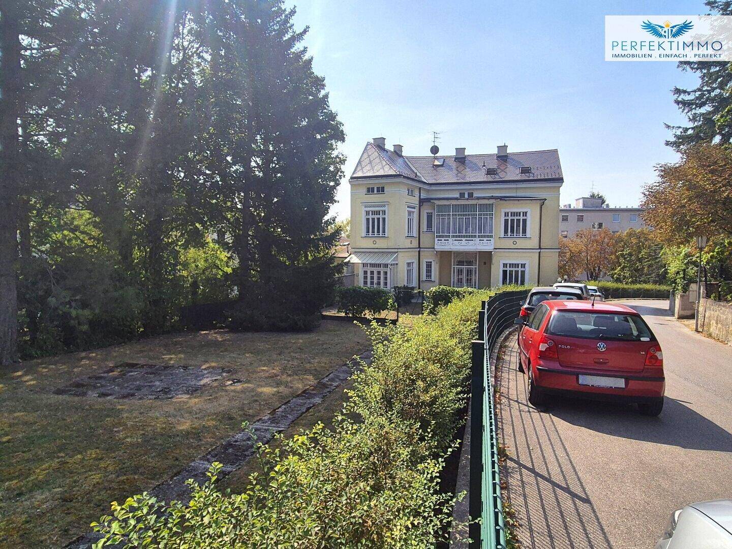 Blick auf die Villa von der Straße aus, umgeben von Bäumen und Grünflächen.