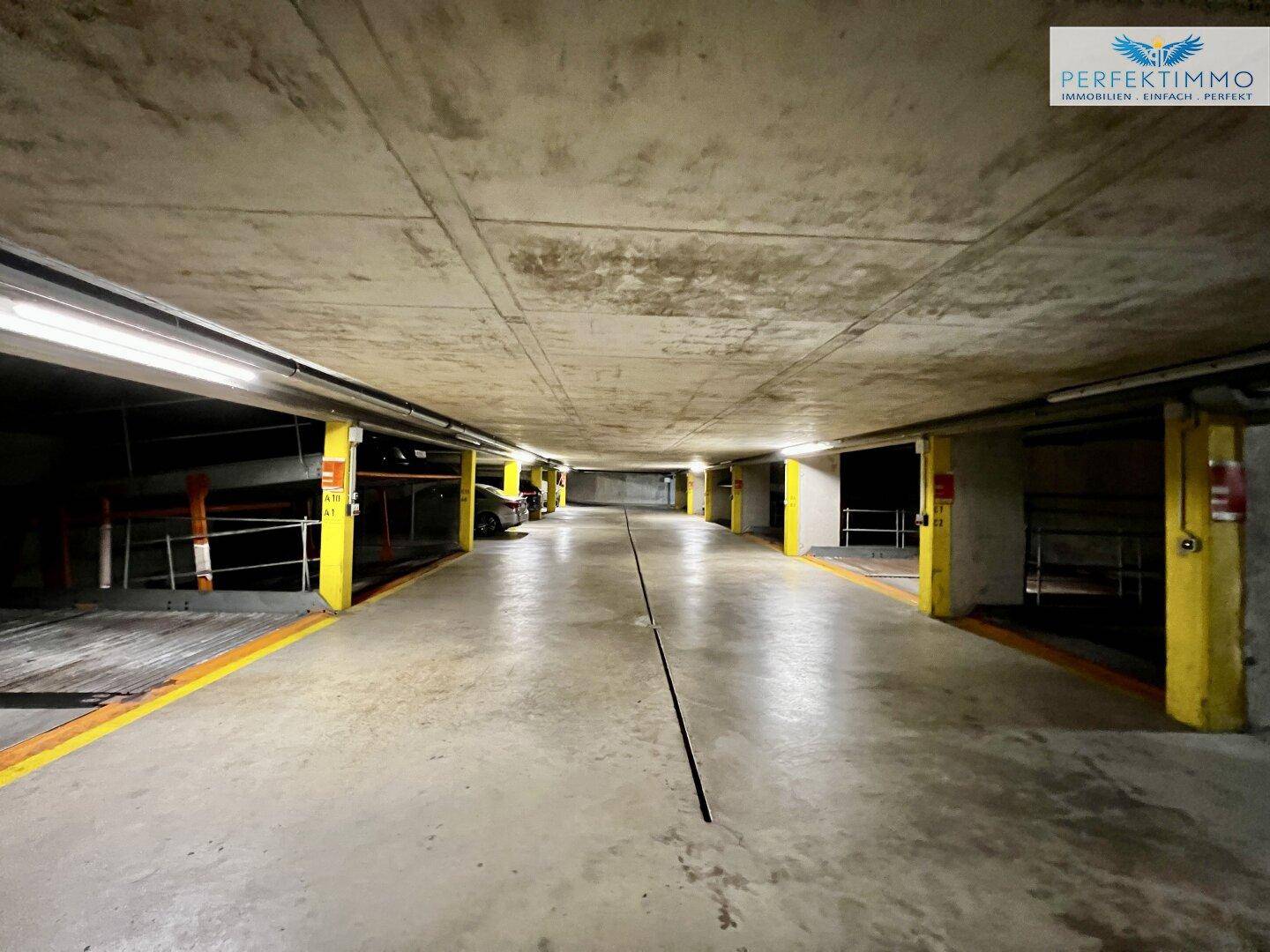 Langer Gang einer Tiefgarage mit zahlreichen Parkplätzen und Betonwänden.