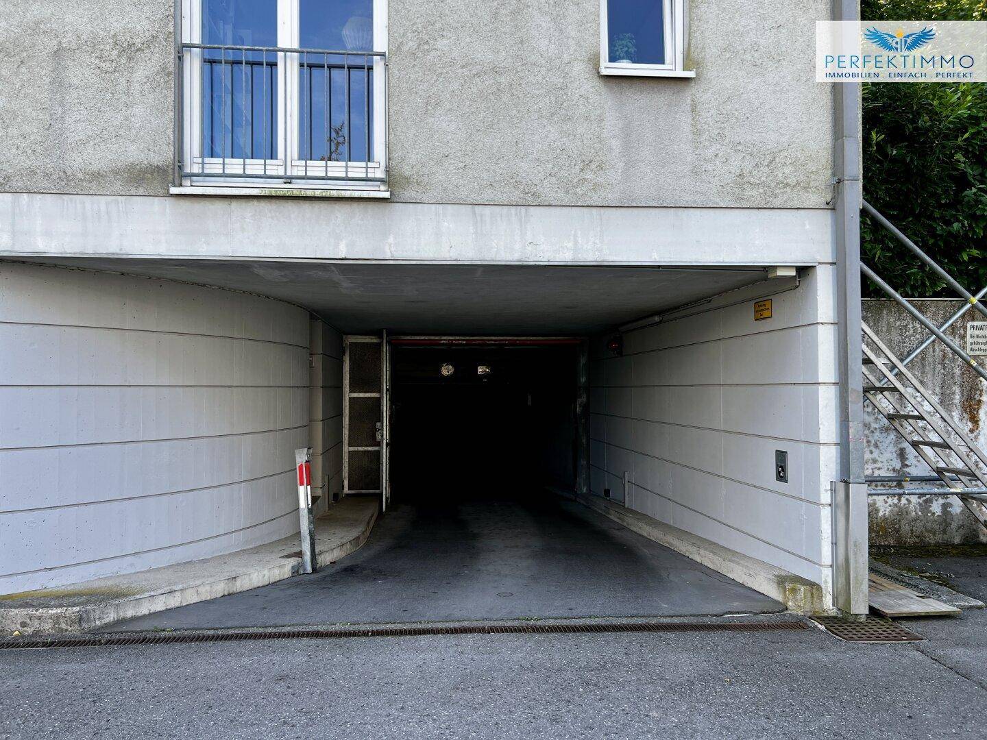 Eingang zur Tiefgarage unter einem Wohngebäude mit Balkon im oberen Bereich.