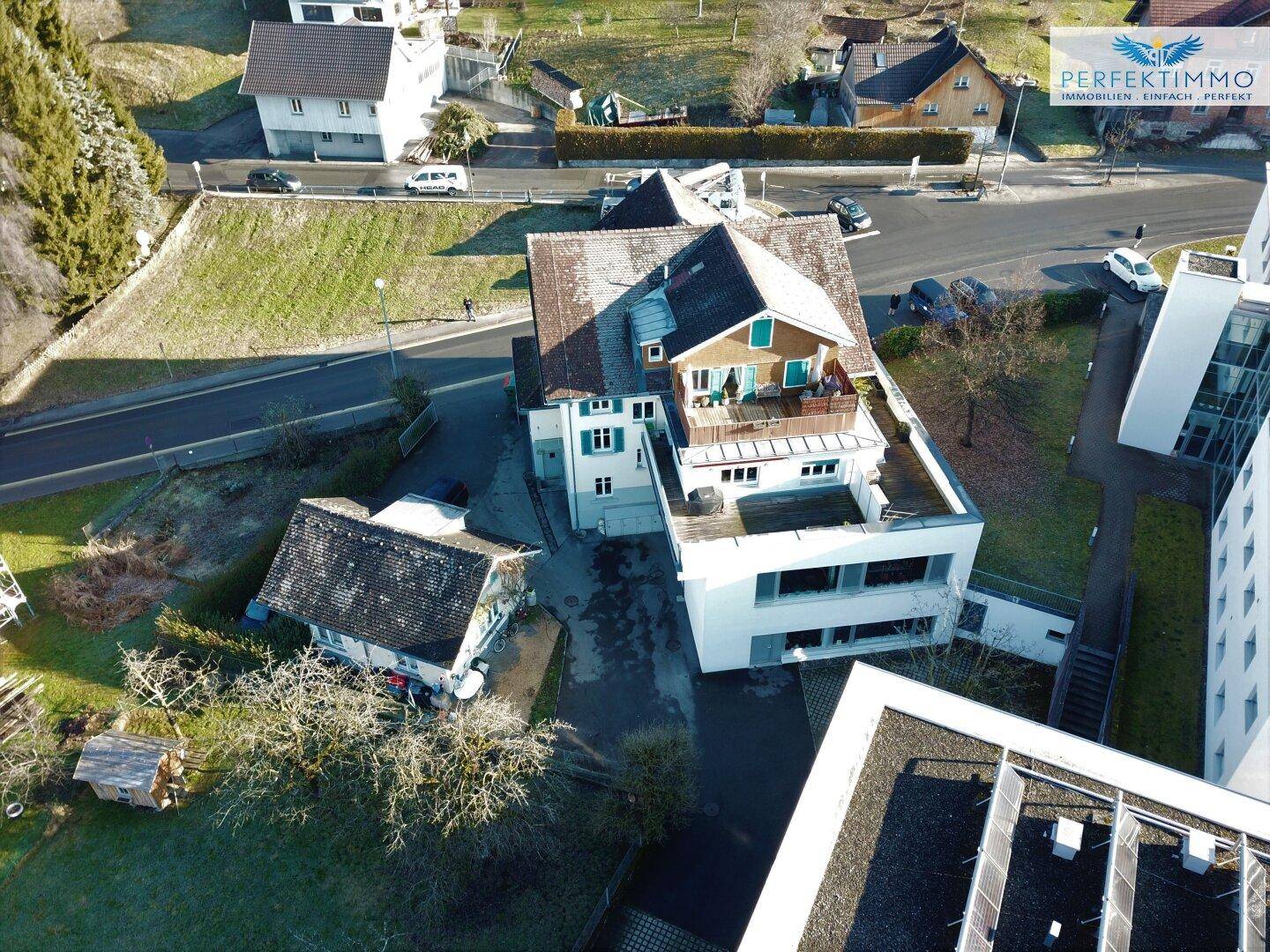 Vogelperspektive eines Wohngebäudes mit angrenzenden modernen Bauten und einer Dachterrasse.