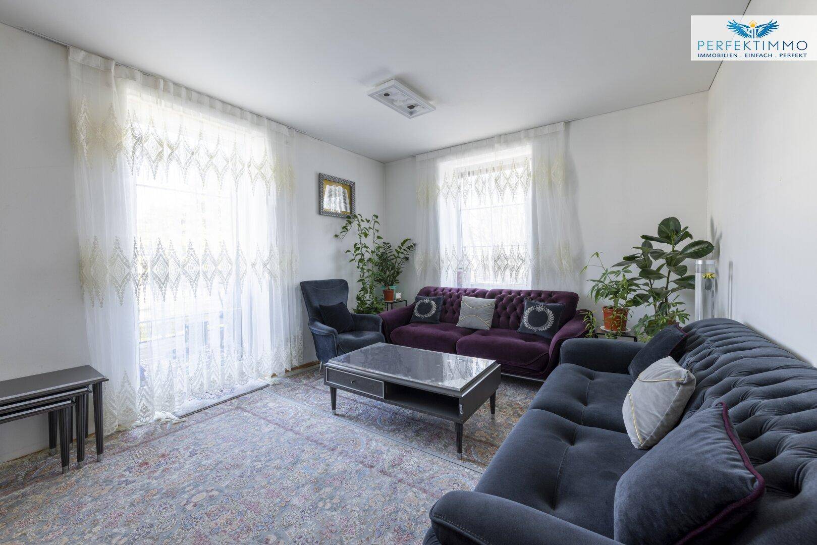 Gemütliches Wohnzimmer mit Teppichboden, bequemen Sofas und großen Fenstern.