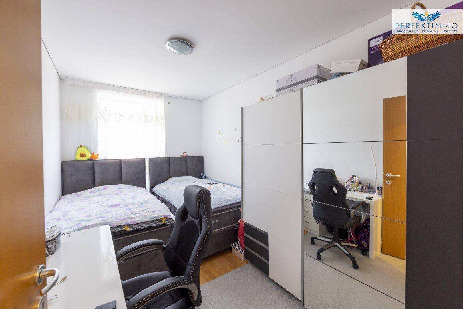 Schlafzimmer mit zwei Betten, Schreibtisch und Kleiderschrank, hell und funktional eingerichtet.
