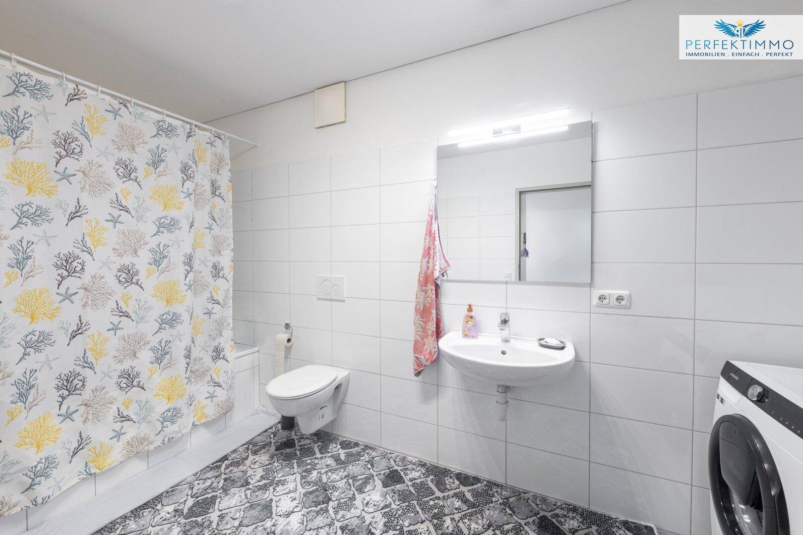 Badezimmer mit Badewanne, WC, Waschbecken und Waschmaschine, hell gefliest.