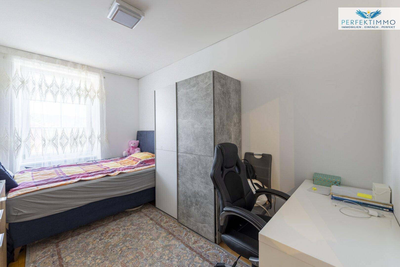 Schlafzimmer mit Einzelbett, Schreibtisch und Kleiderschrank, mit Teppichboden.