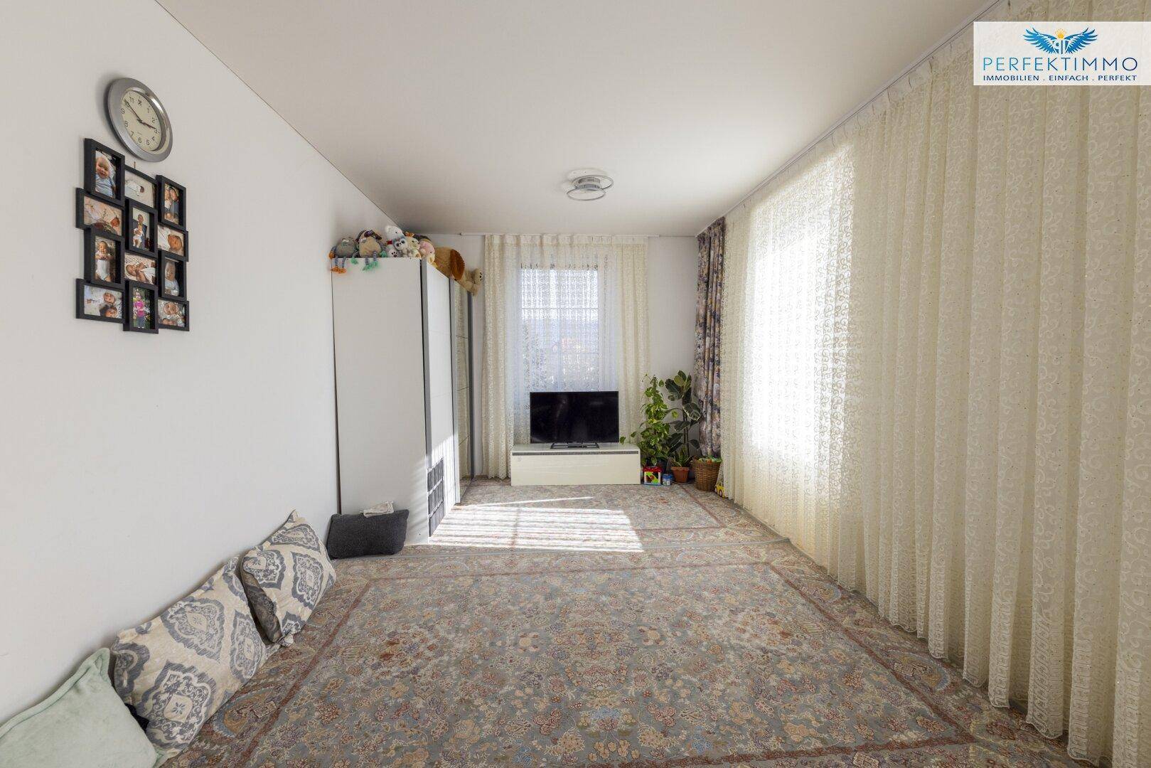 Geräumiges Wohnzimmer mit Teppichboden und großen Fenstern, die viel Licht hereinlassen.