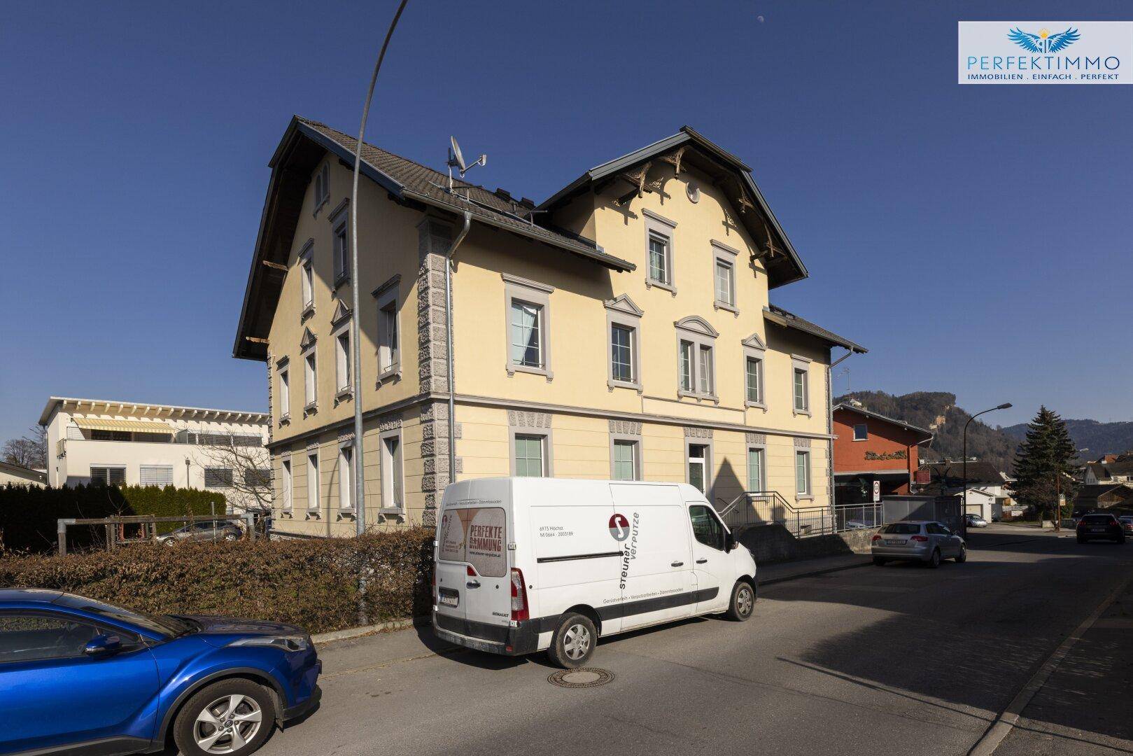 Ansicht des Gebäudes von der Straße aus mit parkenden Fahrzeugen und umliegender Bebauung.