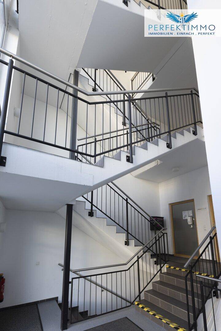 Mehrstöckiges Treppenhaus mit Metallgeländer und Fliesenboden, gut beleuchtet.