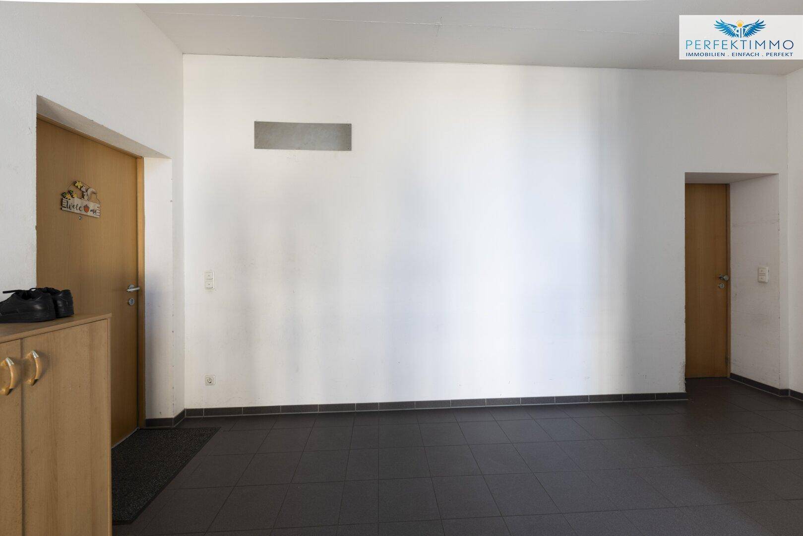 Geräumiger Flur mit hellen Wänden, dunklem Fliesenboden und zwei Holztüren.
