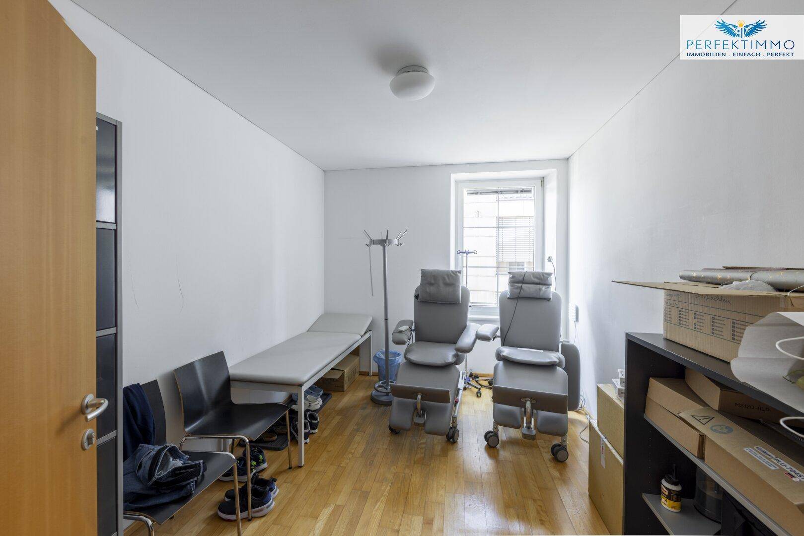 Behandlungsraum oder Büro mit Holzboden, medizinischen Stühlen und einem Fenster.