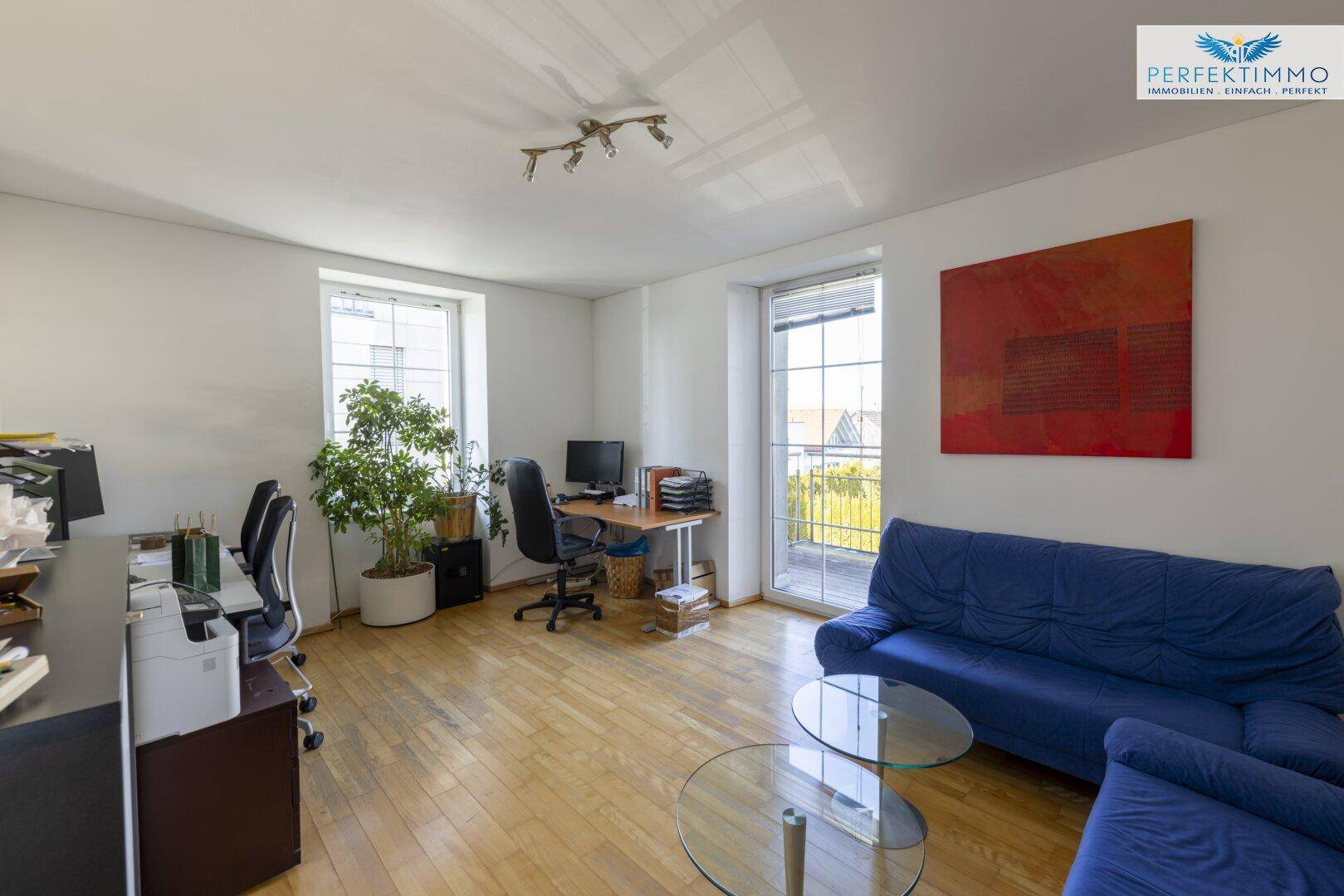 Helles Büro mit Holzboden, blauen Sofas, Schreibtischen und Zugang zu einem Balkon.