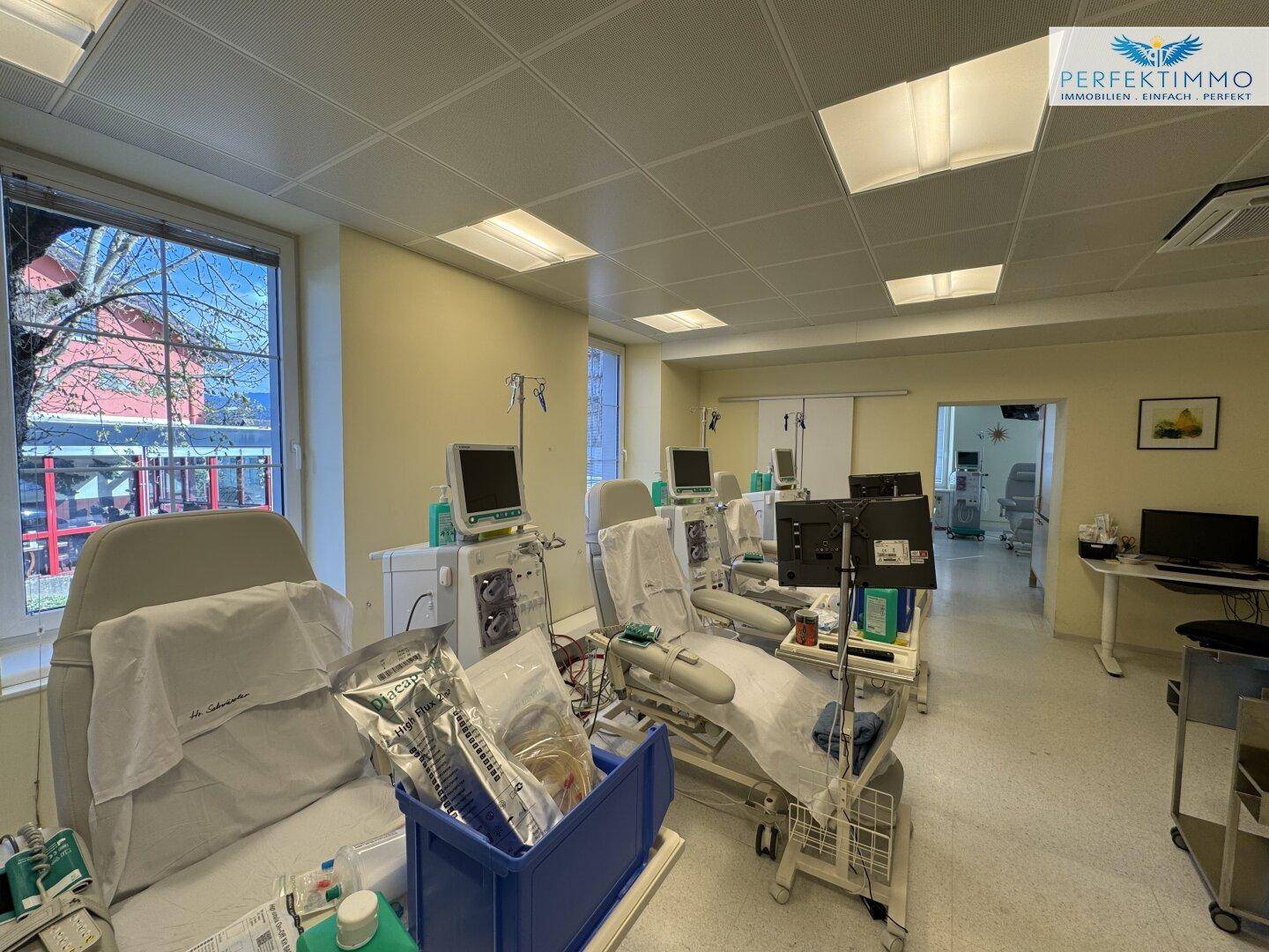 Behandlungsbereich mit Patientensesseln, medizinischen Vorräten und einem Blick nach draußen durch das Fenster.