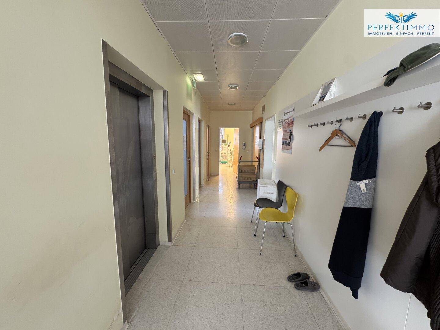 Heller und sauberer Flur mit Fliesenboden, Garderobe und einem modernen Aufzug.
