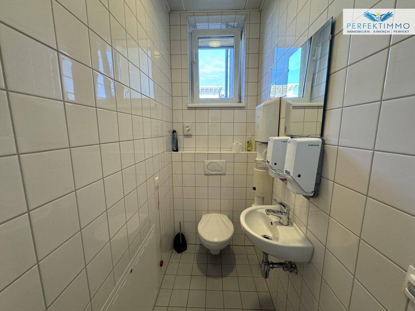 Kleine, geflieste Toilette mit Fenster, Waschbecken und Wand-WC.